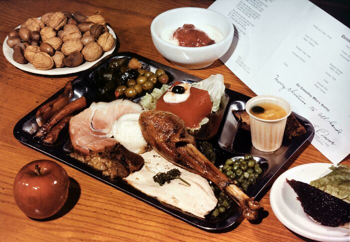 1940 color photos showing a classic dinner with turkey leg, peas, nuts, apple, and dessert on a wooden table.