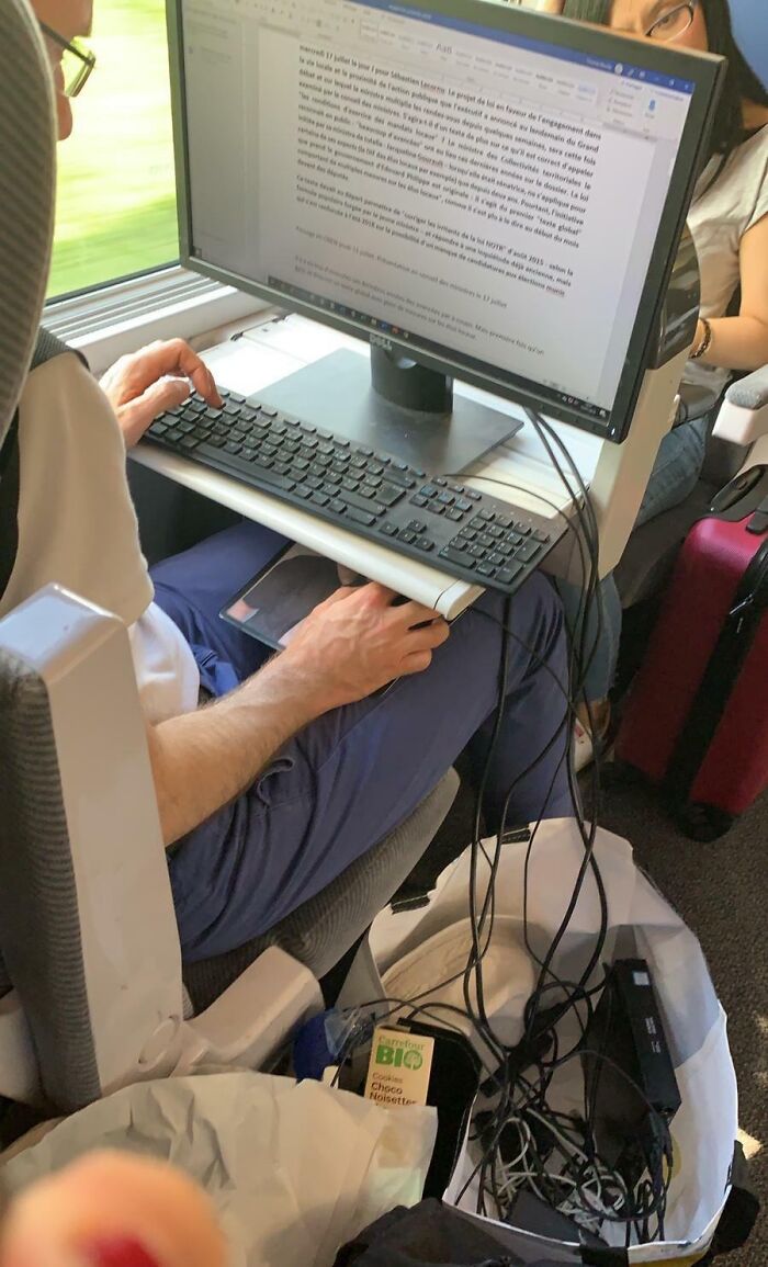 Train passenger using a full desktop setup, including monitor and keyboard, on a subway for a funny scene.