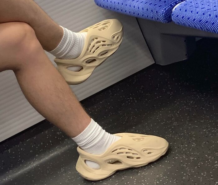 Person in quirky beige shoes sitting on a subway train, showcasing unique passenger footwear style.