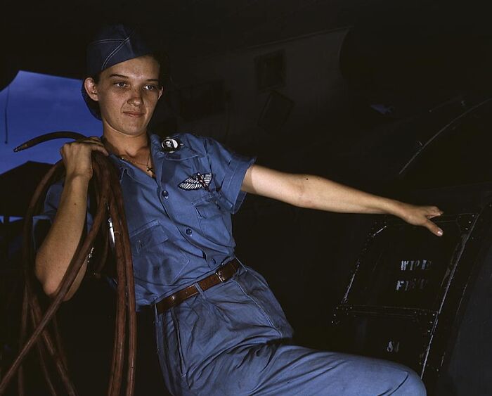 Person in uniform, circa 1940 color photo, holding equipment inside a vehicle with a focused expression.