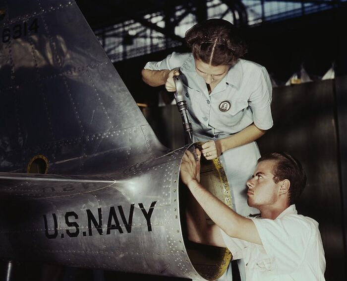 1940 color photo of two workers assembling a U.S. Navy aircraft, showcasing teamwork and industrial effort.