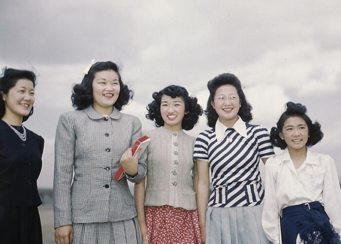 Women in 1940s fashion smiling outdoors, showcasing hairstyles and clothing from the era.