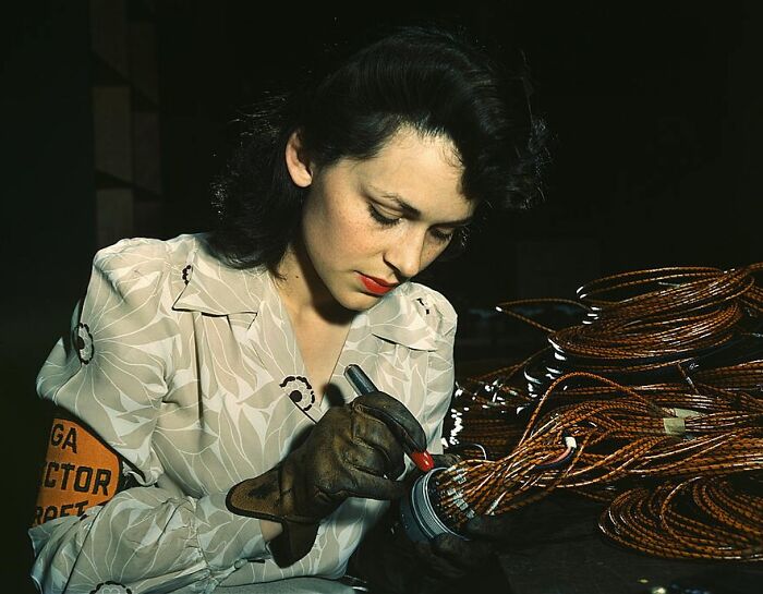 Woman in 1940s attire working with coils of wire, representing 1940 color photos, in a detailed and focused setting.