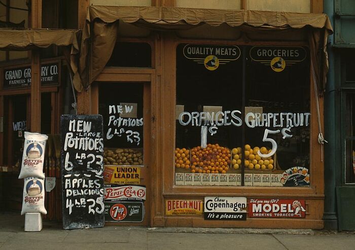 1940 color photo of a grocery storefront displaying fresh produce and vintage advertisements.