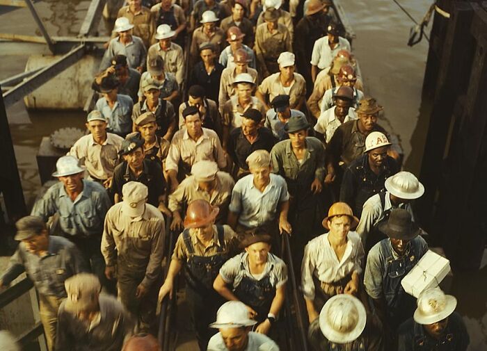 Workers in 1940, captured in color, wearing helmets and work clothes, walk together in a determined group.