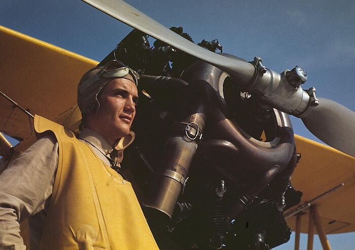 Pilot in World War II attire stands beside a plane, captured in rich 1940 color photos.