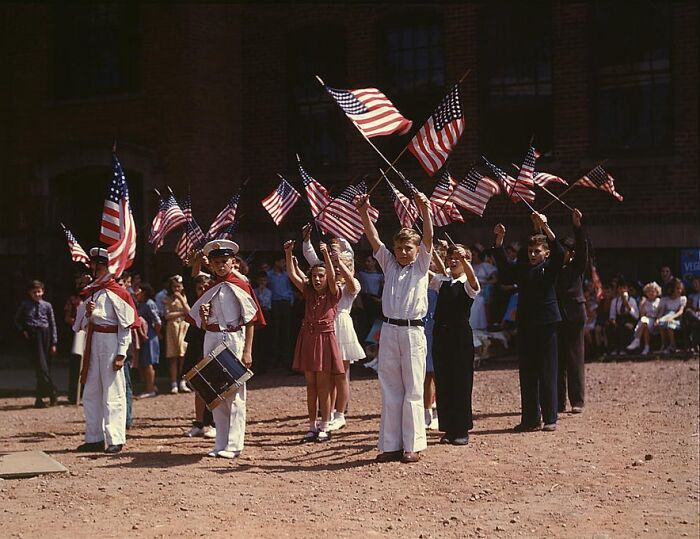 Children in a 1940 color photo parade, waving American flags and dressed in patriotic attire.