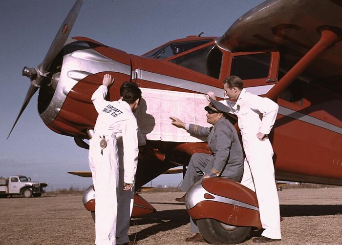 Men in coveralls examine a map on a red airplane in 1940 color photos.