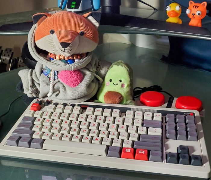 "Retro keyboard with soft toys and colorful desk decor, evoking a nostalgic atmosphere."