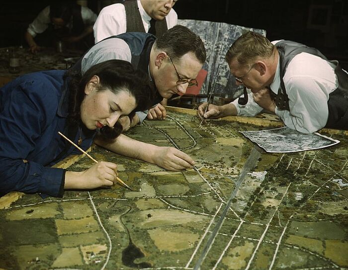 People painting a detailed model landscape in 1940s color photos setting.