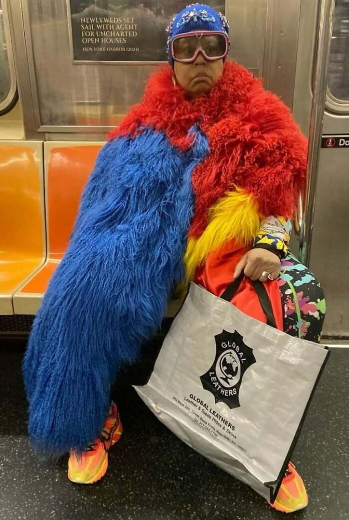 Colorful train subway passenger in a fluffy outfit, wearing goggles and holding a shopping bag, sitting on a subway seat.