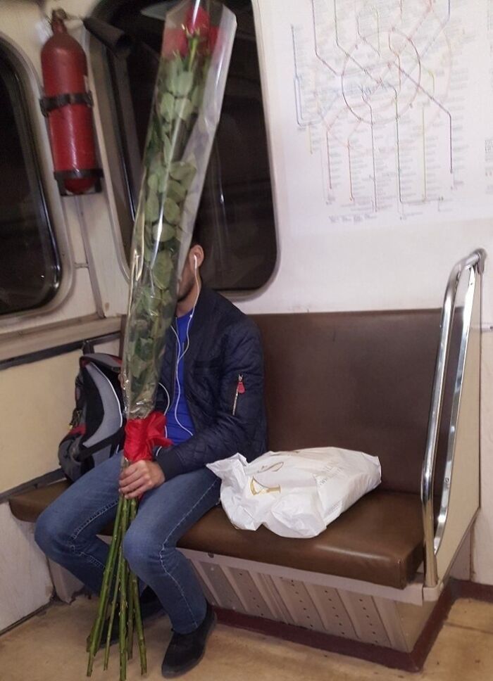 Passenger on subway holding an oversized rose, creating a humorous scene.