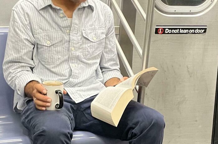 Subway passenger with a book and mug, sitting casually on a train seat.