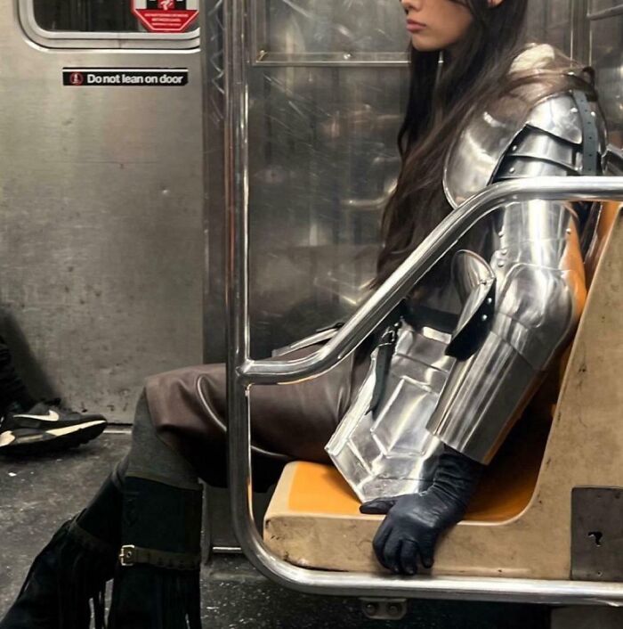 Person in full metallic armor sitting on a subway train seat, showcasing funny train passengers.