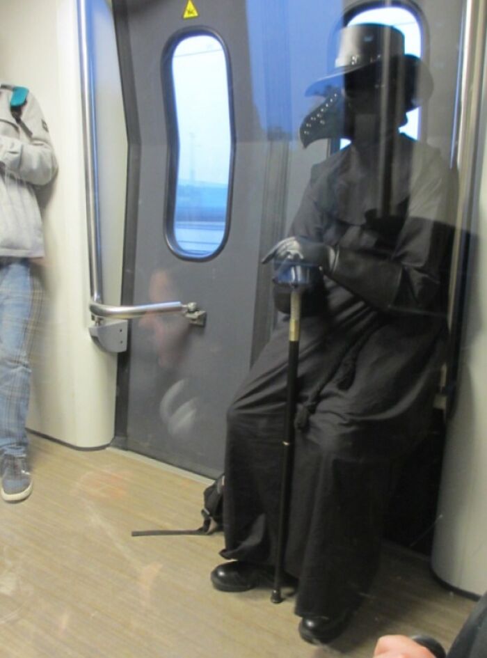 Person in an eccentric costume resembling a plague doctor on a subway train.