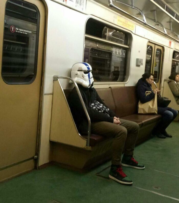 Subway passenger wearing a stormtrooper helmet, sitting on a train.