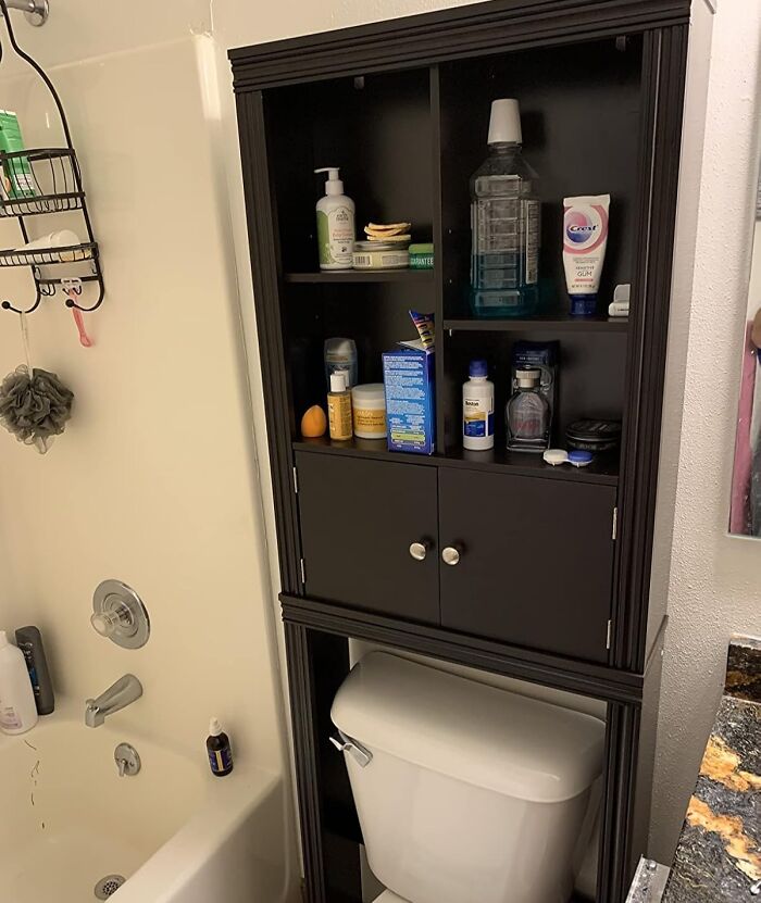 Bathroom products efficiently organized on dark shelving unit above a white toilet.