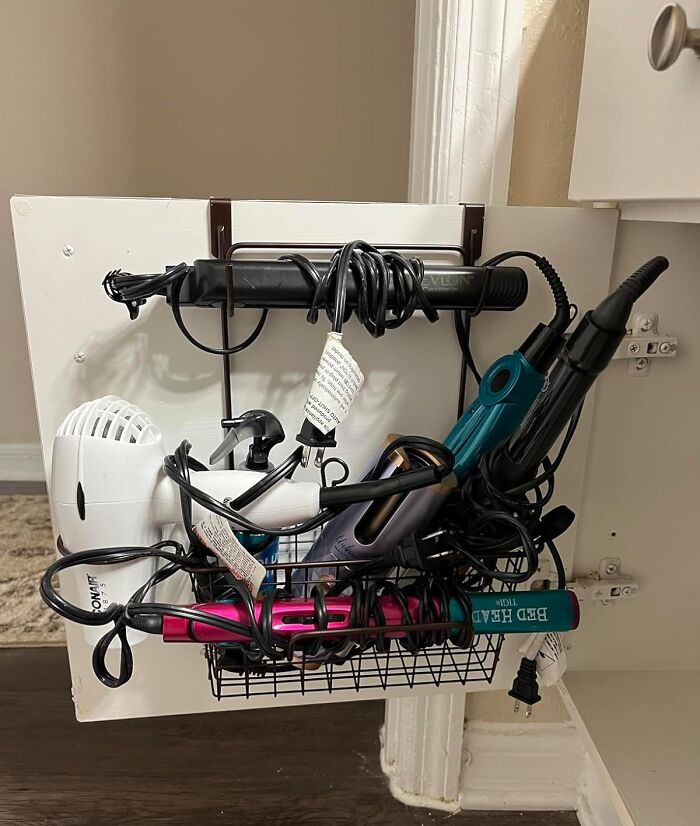 Bathroom products organized in a cabinet drawer, including a hair dryer and curling irons.