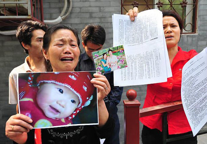 Woman holding a baby's photo and documents, visibly distressed, related to true crime stories and curiosities.