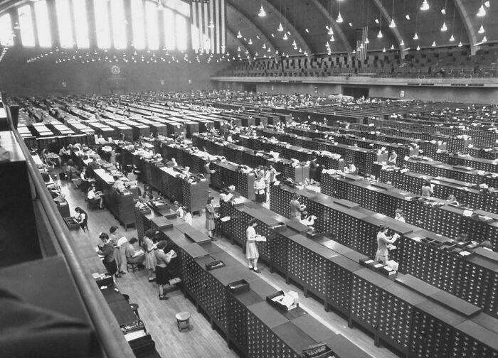 Historic archive room with rows of workers, showcasing true crime curiosities in a vast, organized setting.