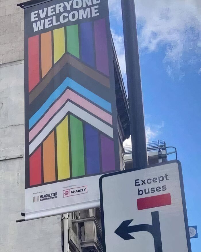 "Colorful ‘Everyone Welcome’ banner in Manchester next to a road sign, capturing a British street scene."