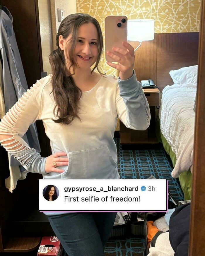 A woman taking a mirror selfie in a hotel room, wearing a casual outfit.