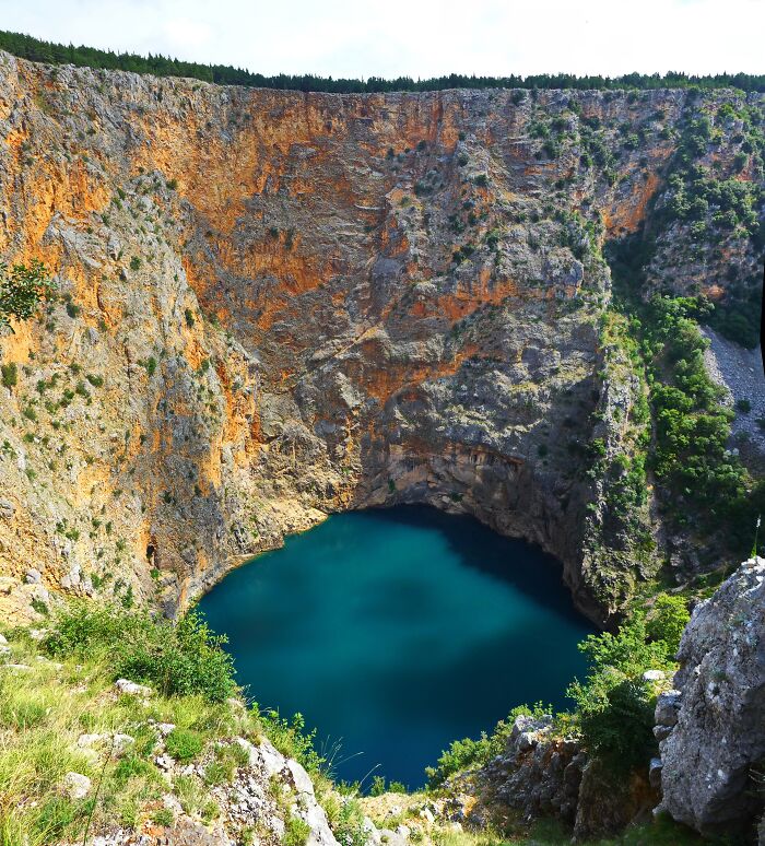 Steep rocky cliffs surround a stunning, tranquil blue lake, showcasing an incredible natural phenomenon.