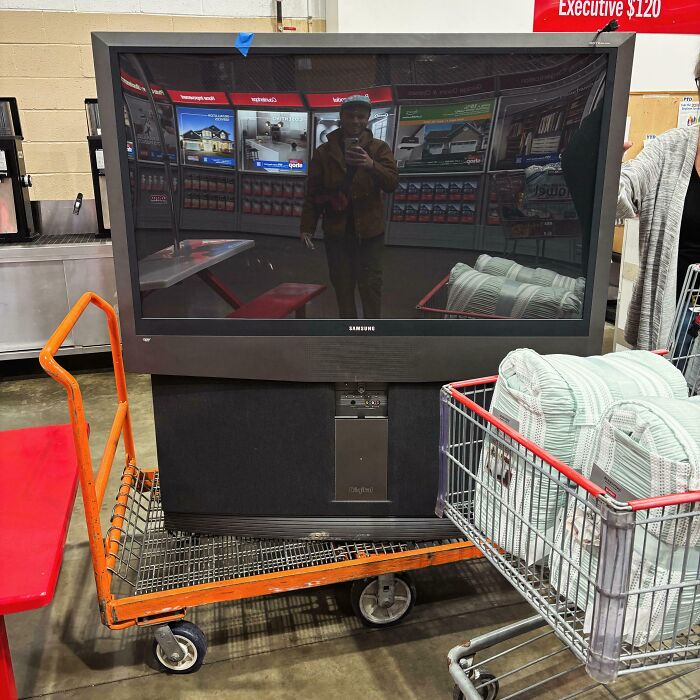 Large TV awkwardly loaded on a shopping cart, people being complete jerks in a store aisle.