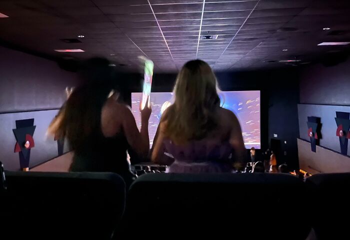 Two people standing and blocking the view in a movie theater, disrupting others.