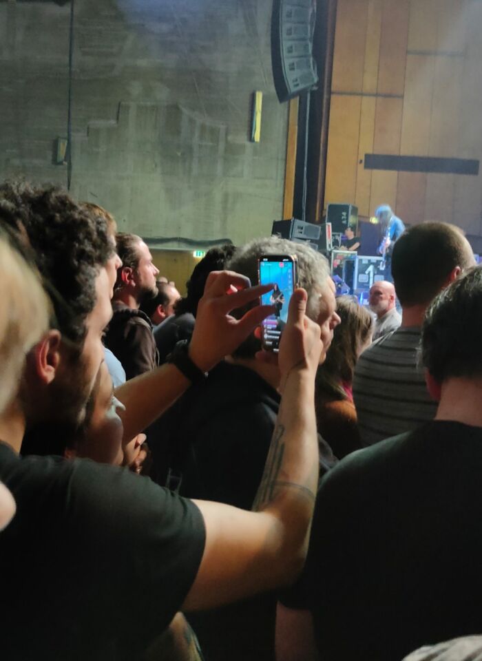 "Person blocking view at a concert, holding a phone, illustrating people being complete jerks in crowded events."