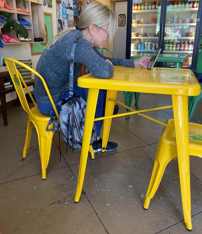 A woman occupies two yellow chairs with a backpack in a cafe, illustrating inconsiderate behavior.