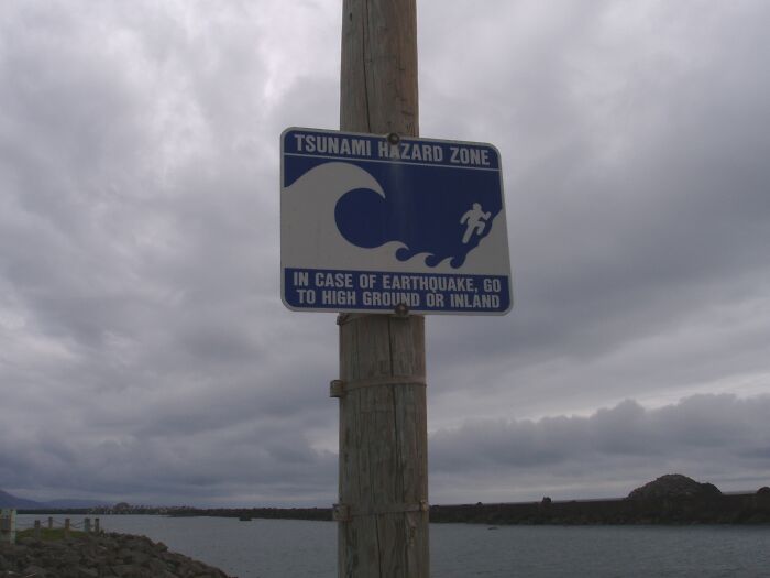 Tsunami hazard zone sign on a pole warns of natural phenomena, advising evacuation to high ground.