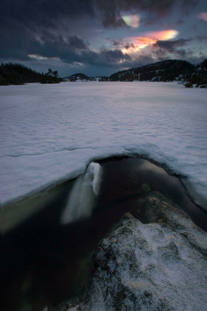 Snow-covered landscape with a colorful, stunning sky phenomenon at dusk.