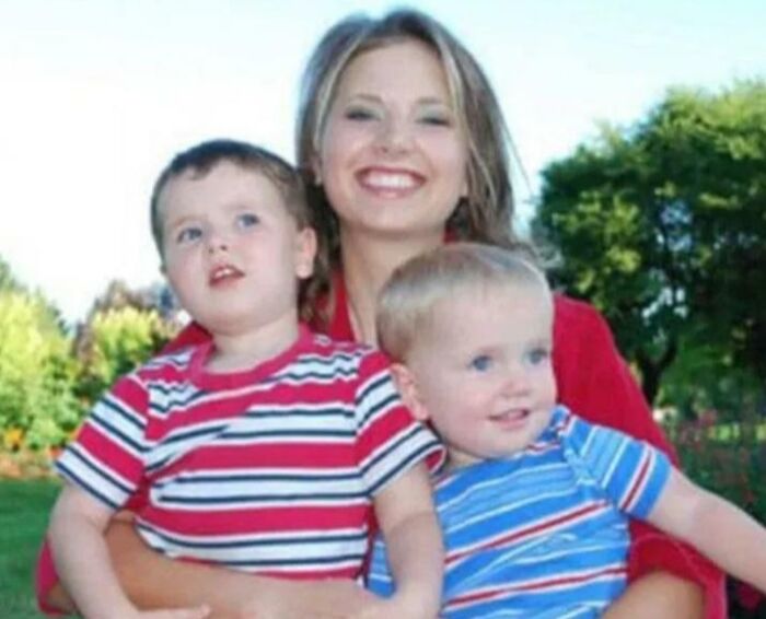 Woman smiling with two young boys in striped shirts, outdoors on a sunny day.