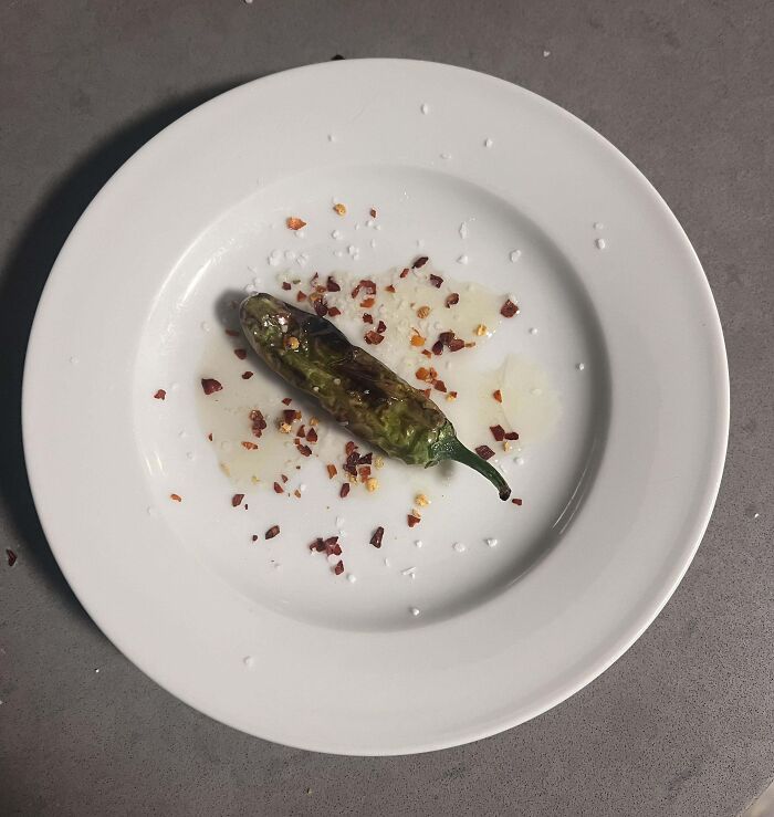 Single tiny pepper on a white plate with crushed red pepper flakes, showcasing a gardening harvest fail.