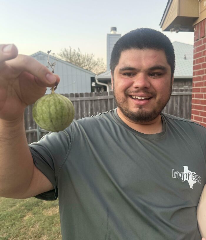 Man smiling while holding a small watermelon, showcasing a gardening fail.