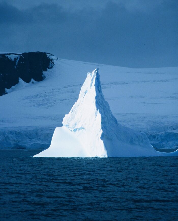 Iceberg towering against a cloudy sky, showcasing stunning natural phenomena in icy waters.