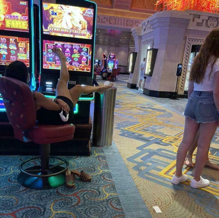 Person lounging at a slot machine with feet up, being inconsiderate in a public casino setting.