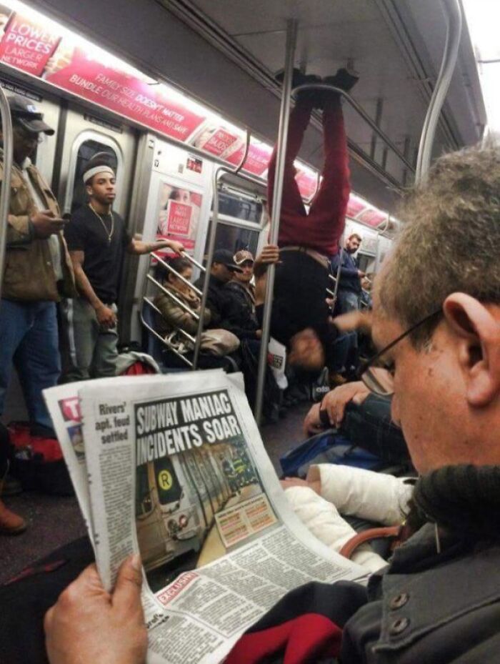 Subway passengers, including one hanging upside down, provide a funny scene as a man reads a newspaper on the train.