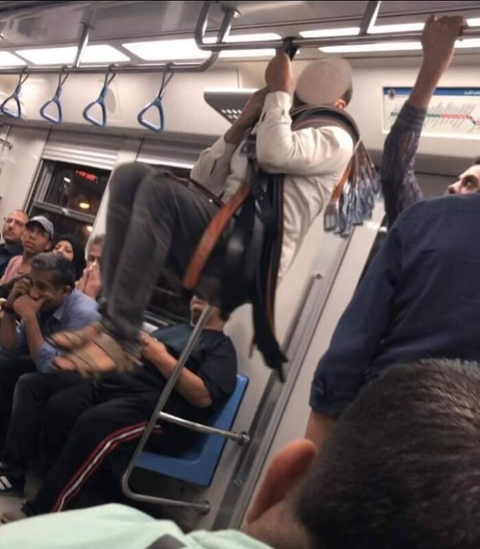 Amusing subway passenger balancing on a baggage platform while others watch with mixed expressions.