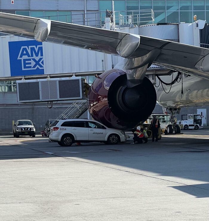 Car wedged under airplane engine, costly incident at airport with staff assessing the situation, highlighting expensive mishap.