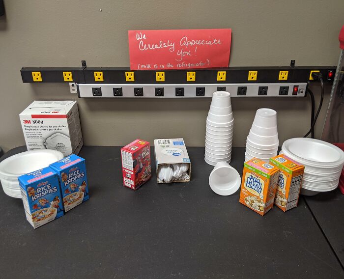 A selection of cereal boxes and bowls on a table with a sign, illustrating infuriating company gifts and bonuses.