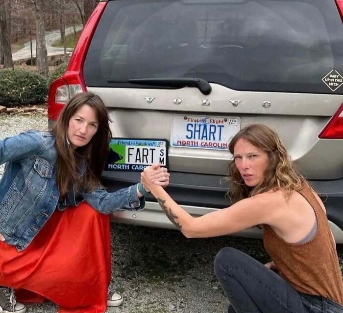 Two women posing with a car; a bizarre license plate reads "FART" next to "SHART" in North Carolina.