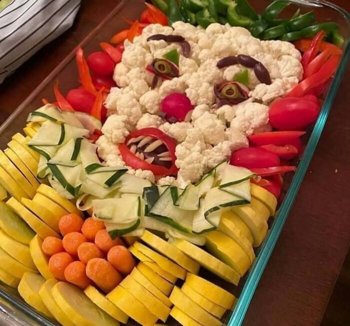 Bizarre food art arrangement resembling a clown face made from vegetables like cauliflower, tomatoes, and carrots.