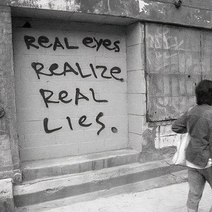 Graffiti on a wall: "Real eyes realize real lies," showcasing a humorous linguistic meme.