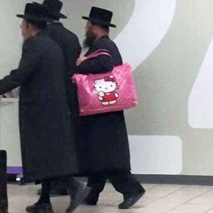 A person in a black outfit carries a pink Hello Kitty bag, showcasing an eclectic style in a bizarre photo.