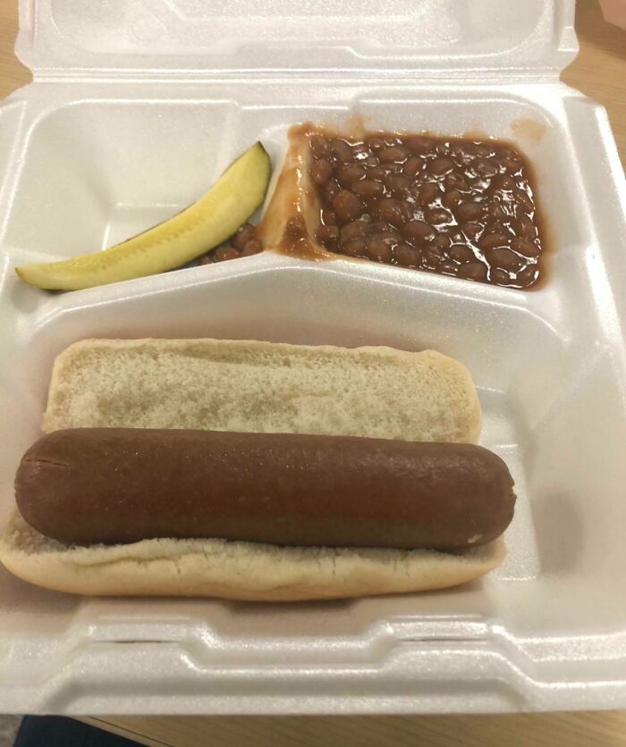 A company gift of a hot dog with beans and a pickle in a foam tray, reflecting an infuriating company bonus.