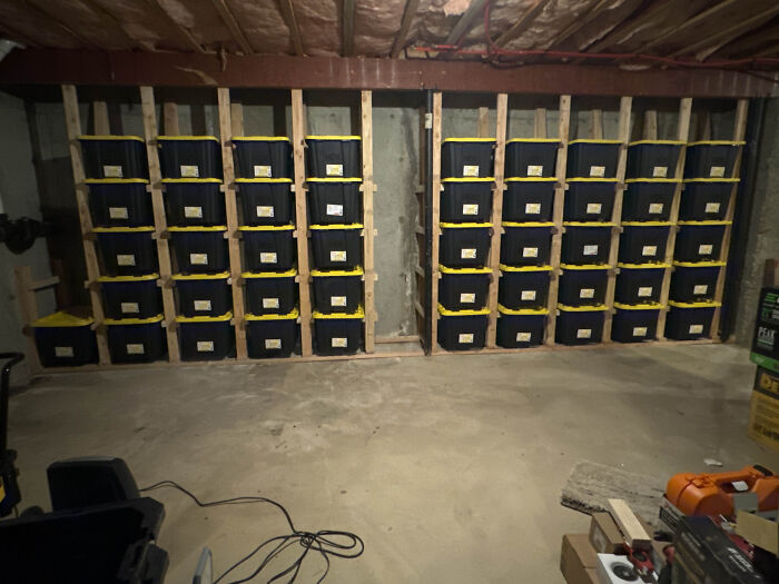 Neat organization of labeled storage bins on shelves in a basement with exposed beams.