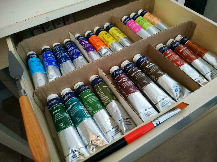 Neatly organized paint tubes in a drawer with a palette knife and brush, illustrating next-level organization.