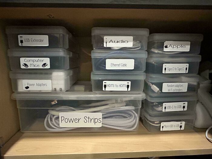 Neat organization of cables and gadgets in labeled plastic boxes on a shelf.